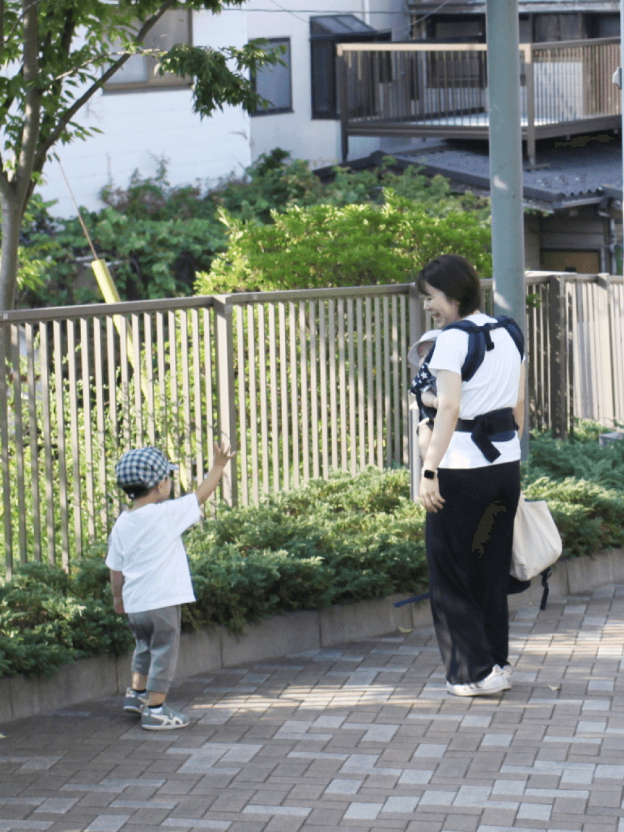 赤ちゃんを抱っこひもで抱えている母親に小さな男の子が話しかけている様子